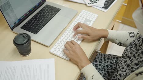 las manos de la mujer de negocios escribiendo en el teclado de la computadora portátil para buscar información, informe de investigación de marketing en el escritorio de la oficina