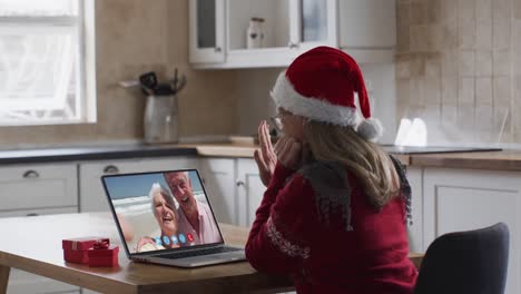 Caucasian-woman-wearing-santa-hat-on-laptop-video-call-during-christmas-at-home