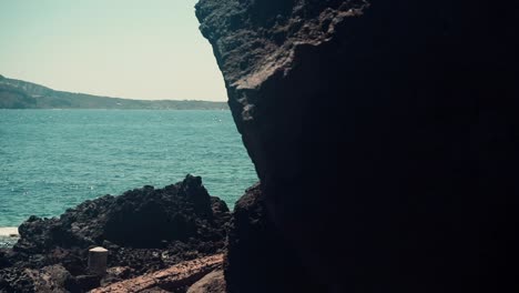 moving forward a volcanic rock formation revealing a beach and a yacht in a greek island during summeritme