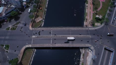 Traffic-bridge-and-overpass-in-Ho-Chi-Minh-City,-Vietnam,-Top-down-aerial-tracking-view-on-a-sunny-day-featuring-the-canal,-rooftops-and-road-traffic