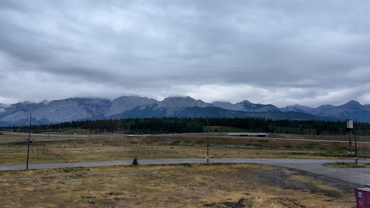 Wide view of Alberta prairie with distant mountains under cloudy sky, rural roadside