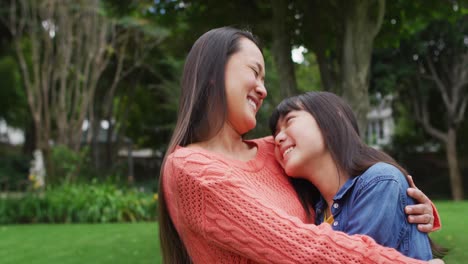 smiling asian mother hugging happy daughter, having fun in garden together