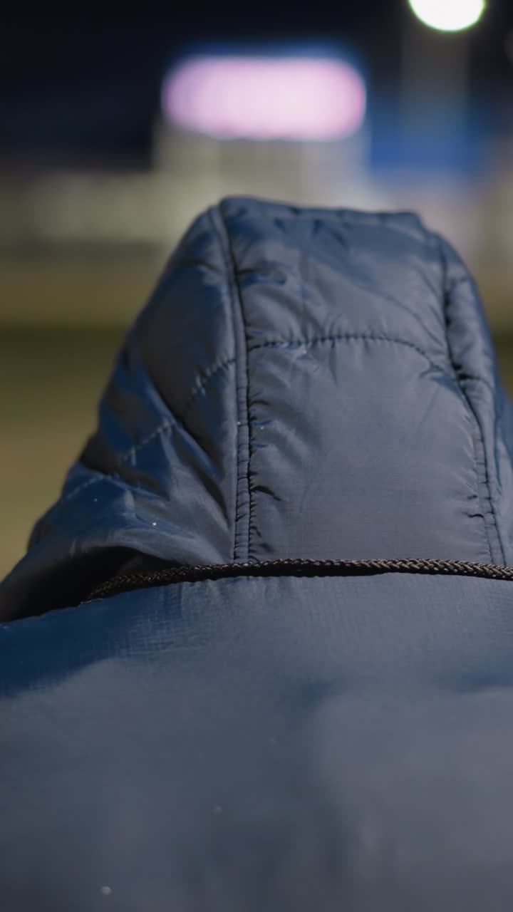 vista de atrás de un hombre con una capucha, sentado solo en un entorno tranquilo, el fondo está borroso y débilmente iluminado