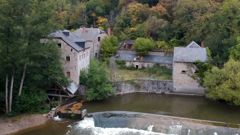 Verlassene-Häuser-Zum-Umliegenden-Wald-Durch-Einen-Flussdamm,-Drohnenaufnahme