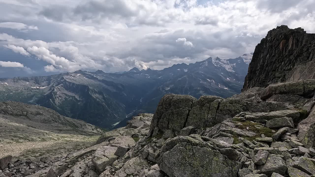 Jagged alpine ridge with large boulders and a moody sky overlooking the Monte Rosa range in Italy.