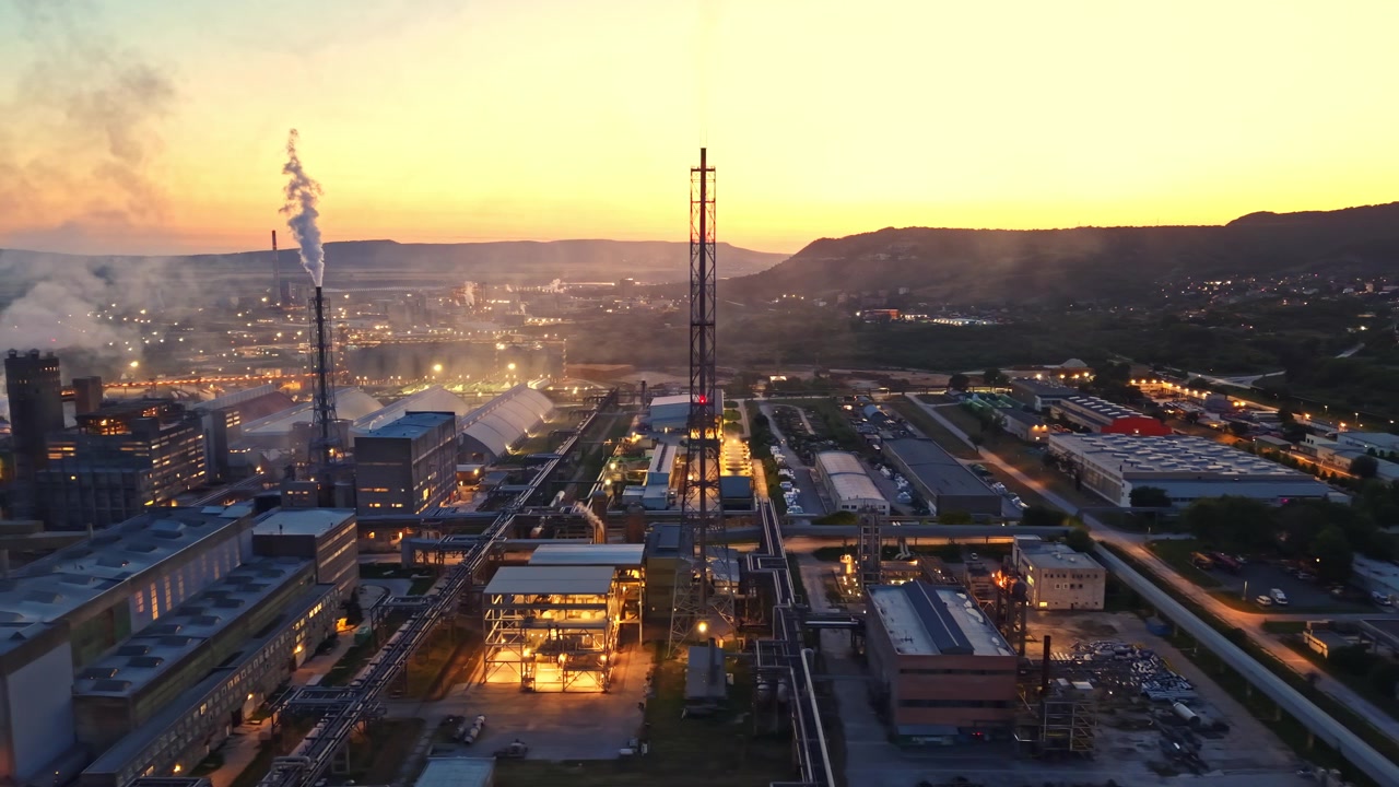 Zona industrial con fábricas y puesta de sol de fondo mostrando humo y luces al anochecer