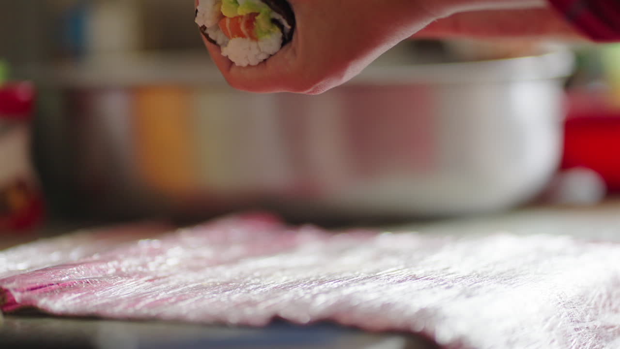 Cook prepares a roll of fresh sushi in kitchen with natural light, close up