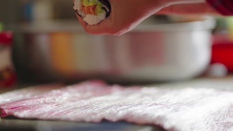 cook prepares a roll of fresh sushi in kitchen with natural light, close up