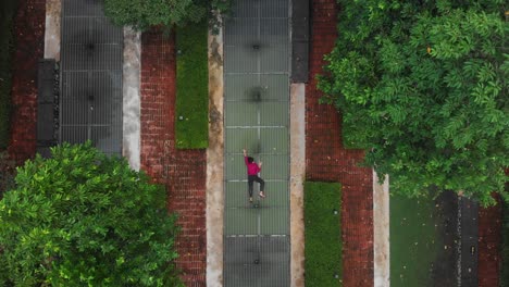 Woman-lay-down-on-ground-between-big-trees-at-Cyberjaya,-aerial