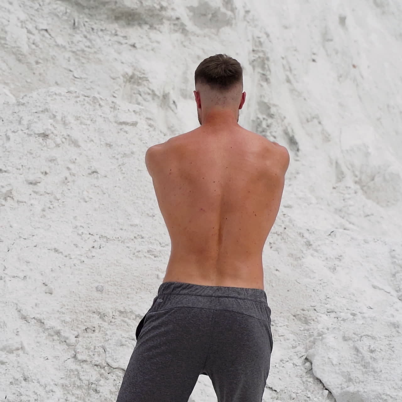 Shirtless bodybuilder in white mountains. Strong man turns back and shows his muscular body outdoors. Slow motion.