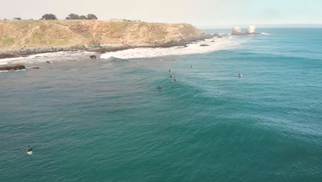 aerial orbit around group of surfers waiting for a wave with rocky formations revealing on the background, pichilemu, chile-4k