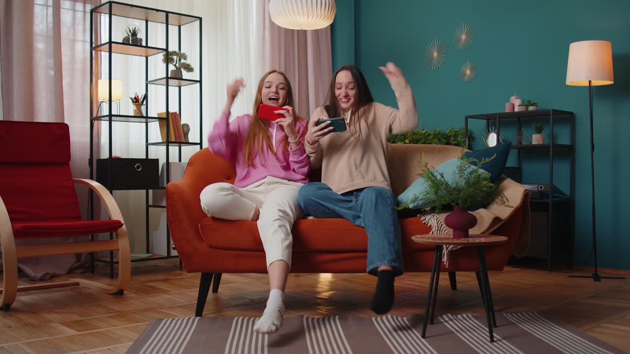 두 명의 재미있는 소녀 친구 형제 자매가 스마트폰에서 열정적으로 경주 비디오 게임을 하고 있습니다.