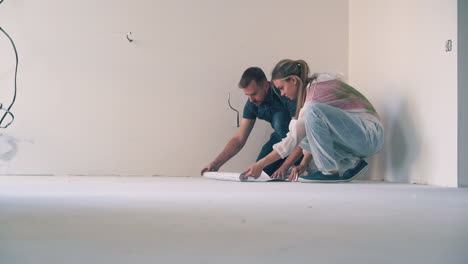 man with wife checks sheet of wallpaper on floor near wall