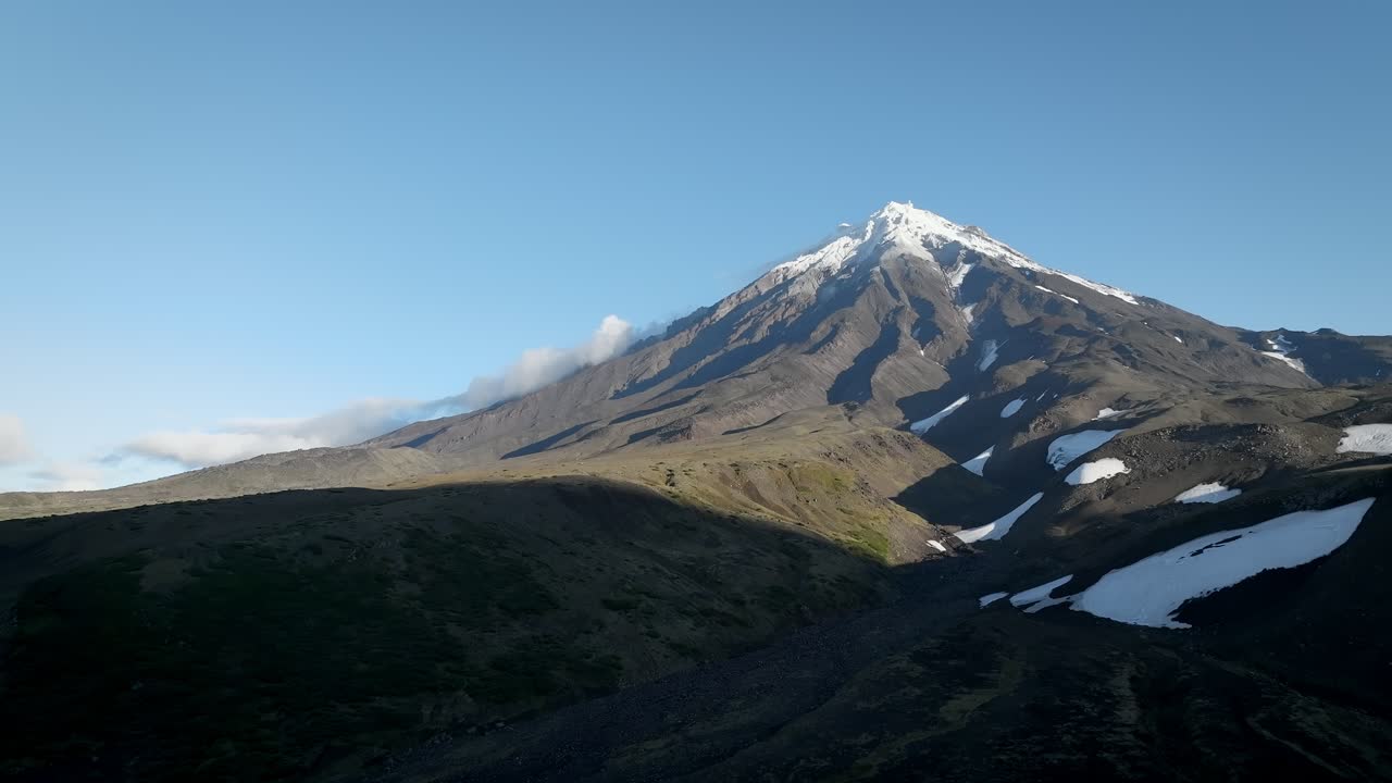 Ampia inquadratura del Vulcano Koryaksky con neve sulla cima e scoscesi pendii vulcanici scuri sotto un cielo limpido, Krai di Kamchatka, Russia, una scena naturale di natura selvaggia remota