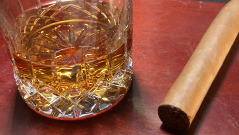 close up of whiskey in glass and cigar sitting on mahogany bar top