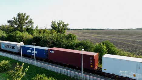 aerial view offreight train with shipping containers traveling through the countryside. the expansive field and surrounding greenery highlight the rural landscape. (4k)