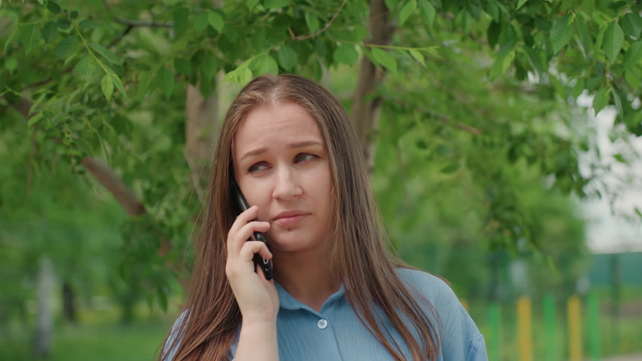 불안한 여성이 야외에서 이야기하고, 걱정하는 여성이 야외에서 강렬한 전화 통화를 하고, 근심에 찬 여성이 장난스러운 배경의 나무들 사이에서 휴대폰으로 통화하고 있어요.