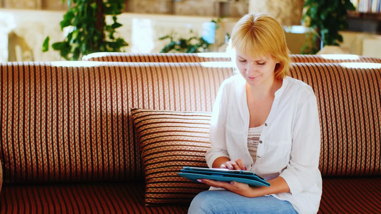 mujer en una camisa de verano usa una tableta en el vestíbulo del hotel