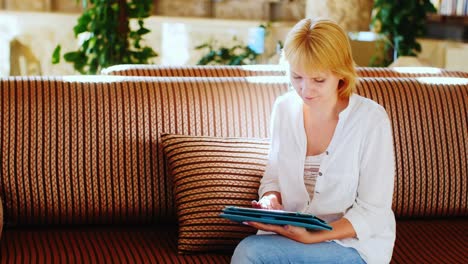 Frau-Im-Sommerhemd-Benutzt-Ein-Tablet-In-Der-Hotellobby