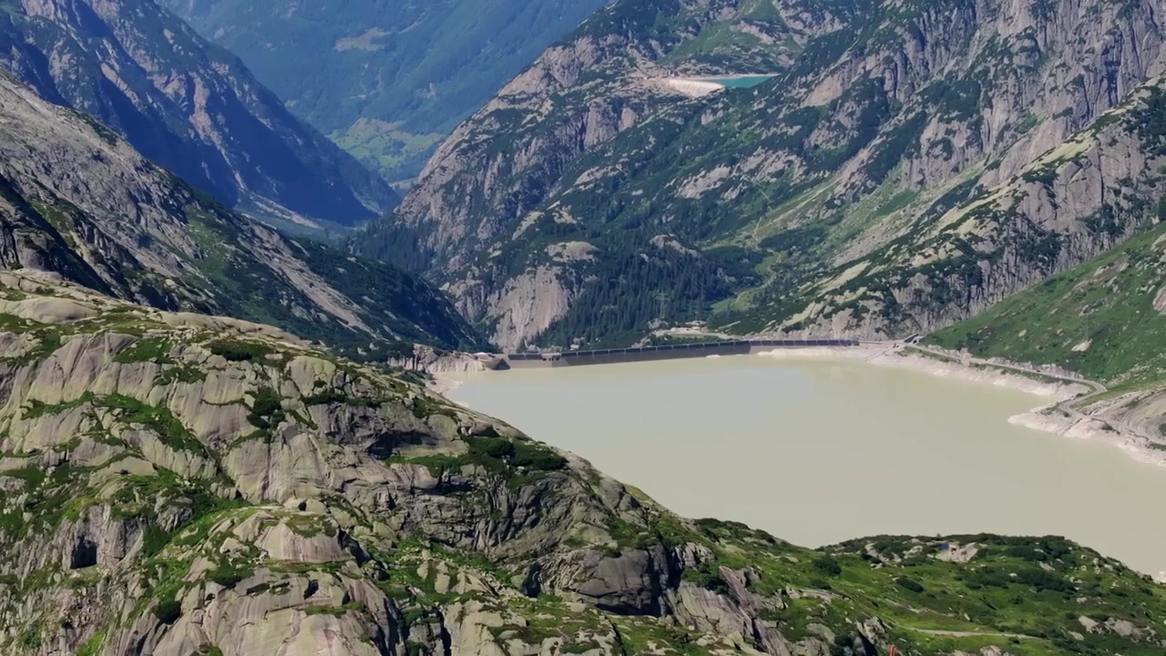 Telefoto fra luften rammer inn blekt vannreservoar under granitttopper i de barske sveitsiske alpene