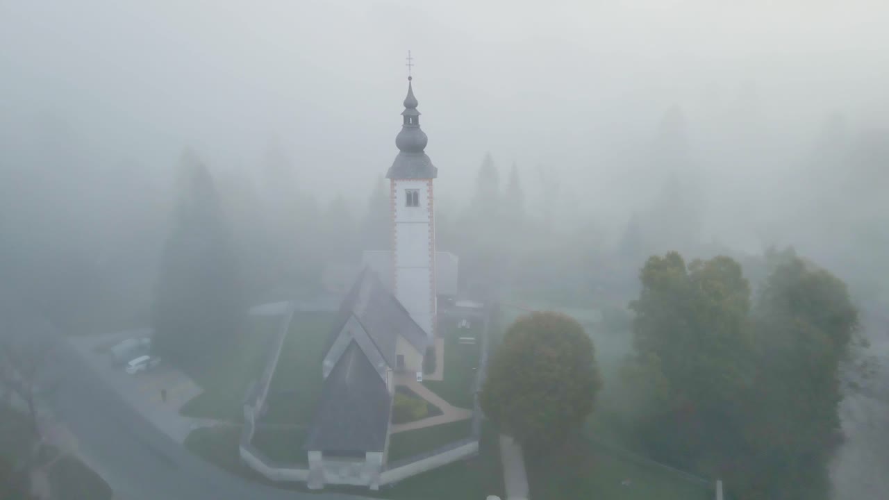 Smukt luftfoto af tåget skov og kirke ved den fredfyldte Bohinjsko Jezero, Slovenien