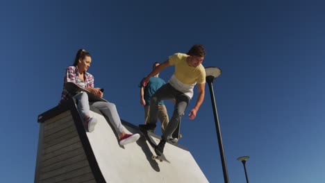 happy caucasian woman and two male friends skateboarding on sunny day