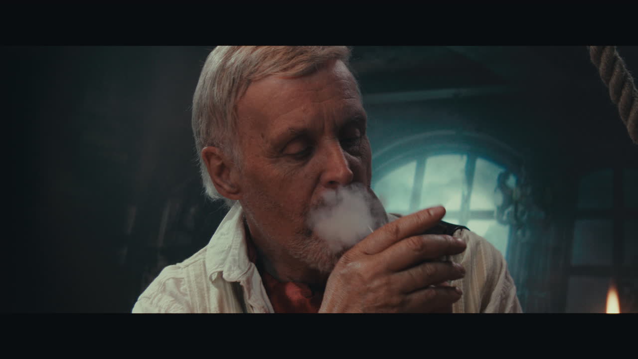 An old pirate eats and drinks and smokes a pipe inside the sailing ship cabin