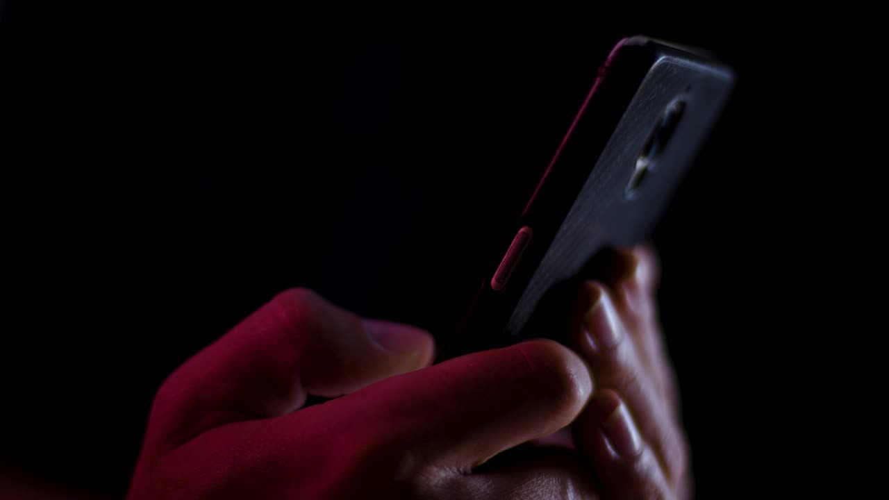 Thumb scrolling on a smartphone close up in a dark room with red and white lighting