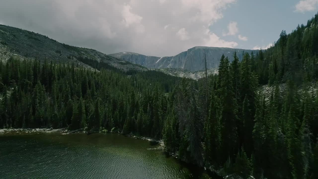 antena del lago en la cuenca de montañas cubiertas de pinos y en la distancia picos nevados