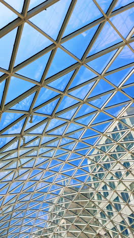 urban modern architecture. a geometric glass structure reflects blue sky and sunny weather over an urban landscape, showcasing innovative design