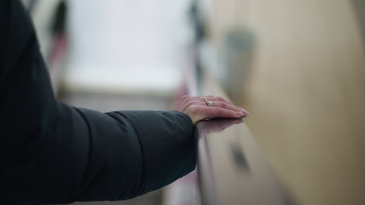블랙 후디를 입은 손이 움직이는 에스컬레이터 레일에 누워있는 클로즈업, 반지로 장식, 배경은 손과 주변에 미묘한 초점을 맞추고 흐릿합니다.