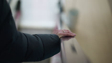 primer plano de la mano con capucha negra descansando en el riel de la escalera mecánica en movimiento, adornado con anillos, el fondo está borroso con un enfoque sutil en la mano y los alrededores