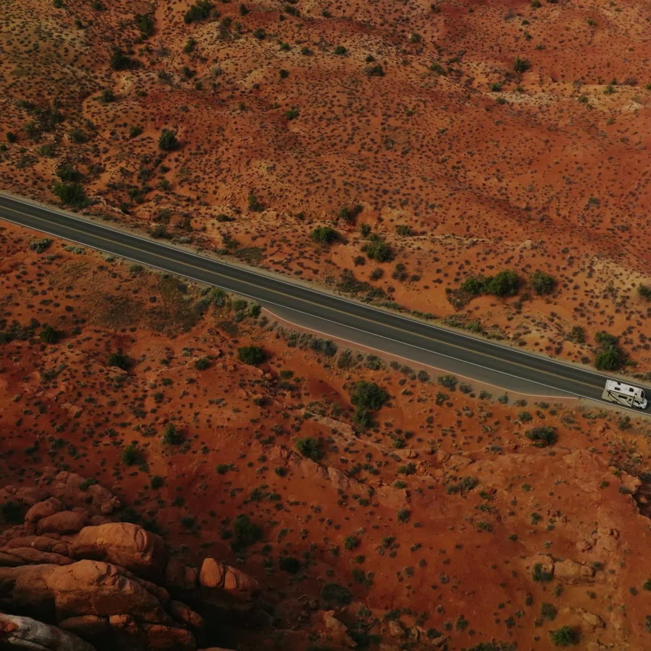 White trailer going by the road in the deserted land of Utah, USA. Drone footage over the sandy land and rounded rocks of canyons. Atop view