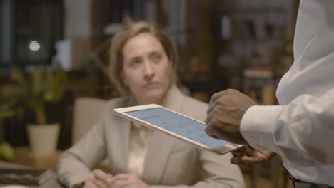 close up view of unrecognizable american man employee holding a tablet and explaining graphics to female coworkers who are sitting at desk in the office