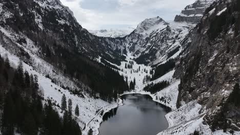 Eine-Luftaufnahme-Zeigt-Die-Ruhe-Des-Tahlalpsees-In-Filzbach,-Glarus-Nord,-Schweiz,-Mit-Schneebedeckten-Berggipfeln,-Die-Den-Ruhigen,-Im-Tal-Eingebetteten-See-Umarmen,-Natürlicher-Schönheit-Und-Ruhe