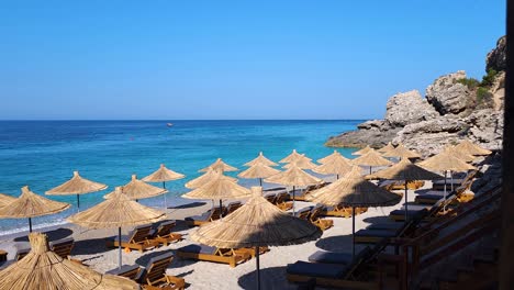 Paradise-beach-with-straw-umbrellas-and-loungers-on-sand-beach-at-sunrise,-beautiful-summer-vacation-on-seaside-of-blue-Mediterranean