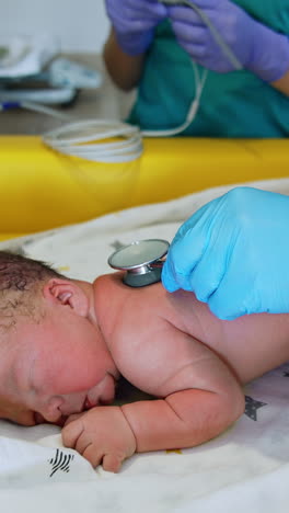 adorable newborn naked baby lies on the belly. neonatologist listens to child's heart with stethoscope. vertical video