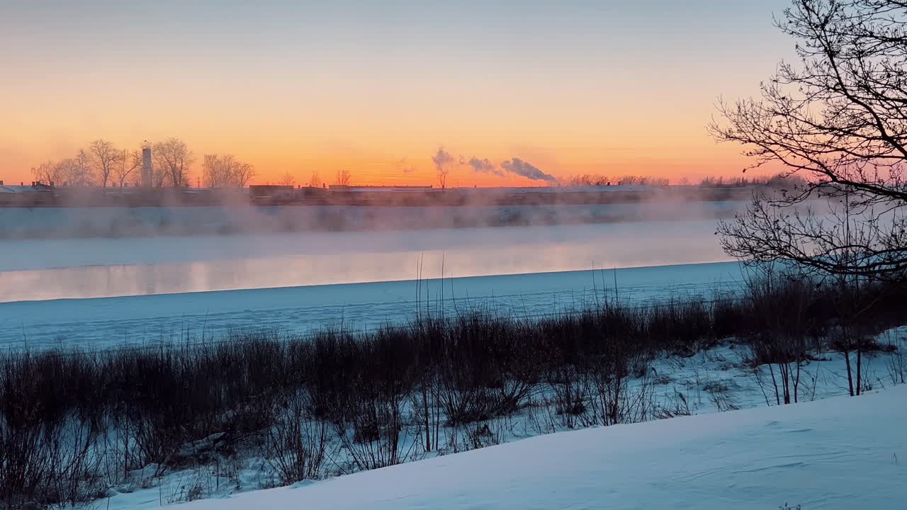 Beautiful winter landscape with a frozen river emitting frost smoke during a cold, colorful sunset, creating a serene and picturesque scene