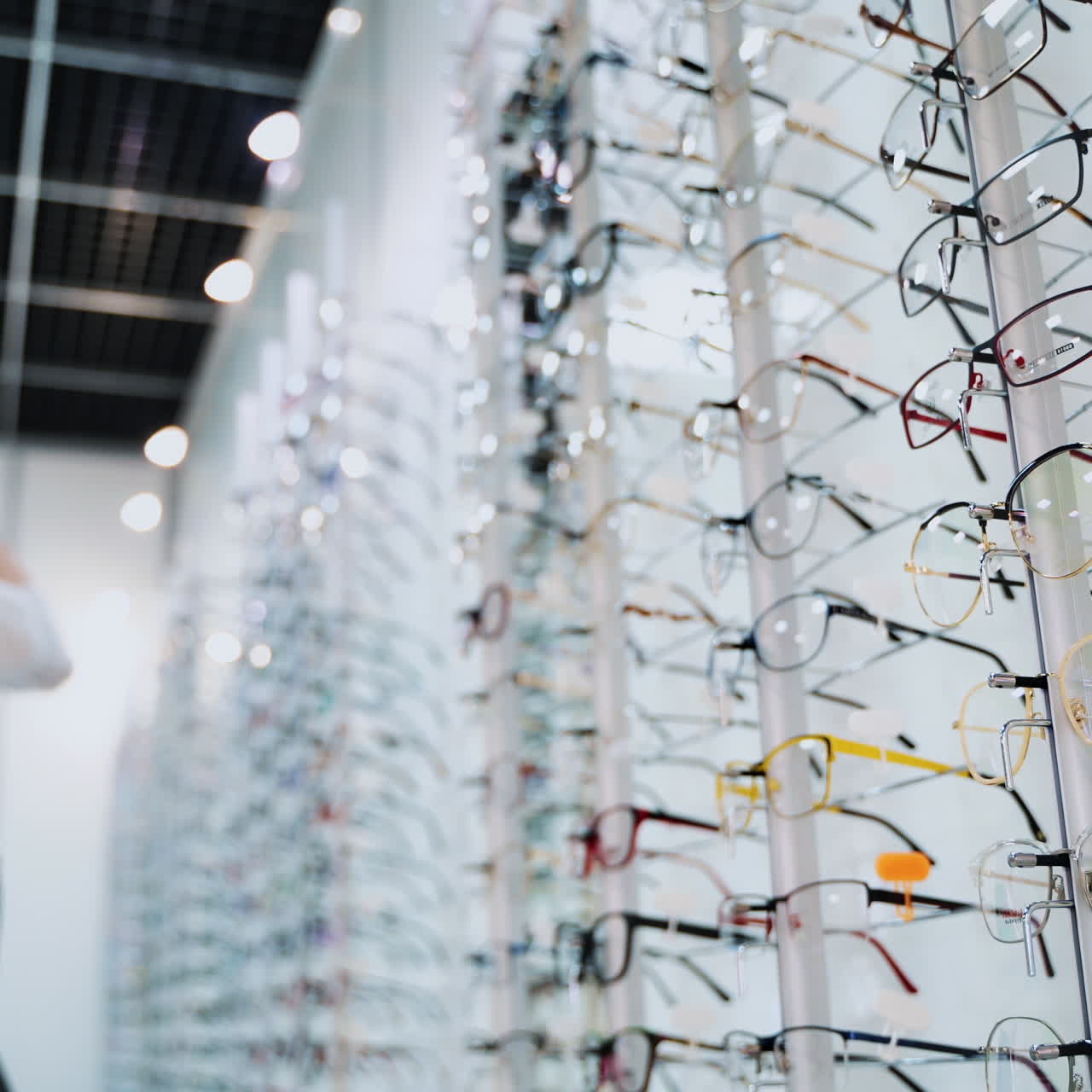 Close-up glasses on the stand on the blur background with customer. Fashionable eyeglasses in the optical store. Vision concept.