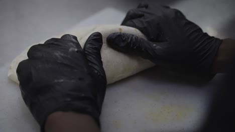 folding chicken wrap in close up, chef hands in black gloves