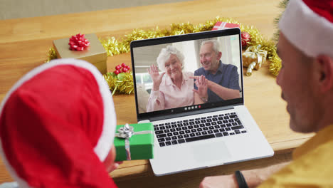 Caucasian-father-and-son-with-santa-hats-using-laptop-for-christmas-video-call-with-couple-on-screen