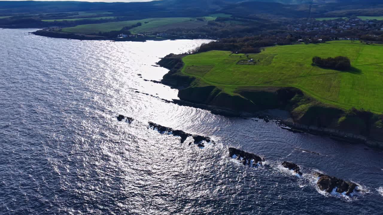 Serenità costiera con onde luccicanti e vibranti campi verdi sotto il cielo azzurro e rilassante a mezzogiorno