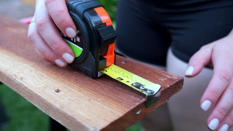 slow motion of woman's hands rolling out measuring tape on wood, woodworking outdoors in daytime