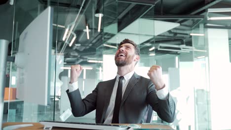 joven empresario guapo y alegre sentado en un escritorio, trabajando en una oficina moderna, arrojando dinero por encima de su cabeza