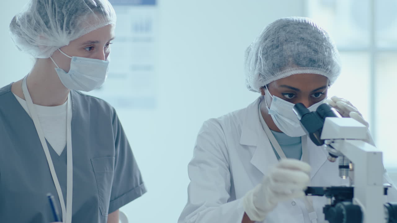 Vrouwelijke wetenschapper gebruikt microscoop en doet laboratoriumonderzoek met assistent.