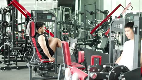 Two individuals engage in a focused leg press workout in a well-equipped Bangkok gym, showcasing determination and fitness