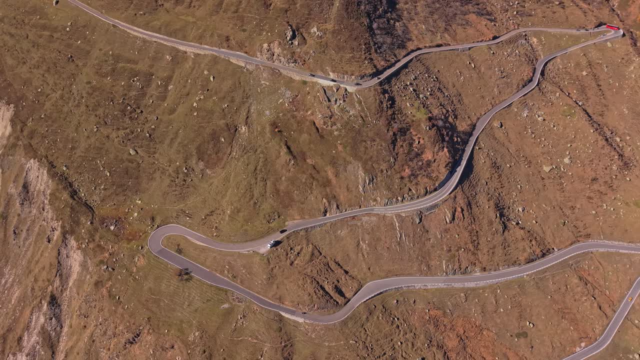 Il traffico scorre in una giornata di sole sul Passo della Furka, con paesaggio alpino sullo sfondo.