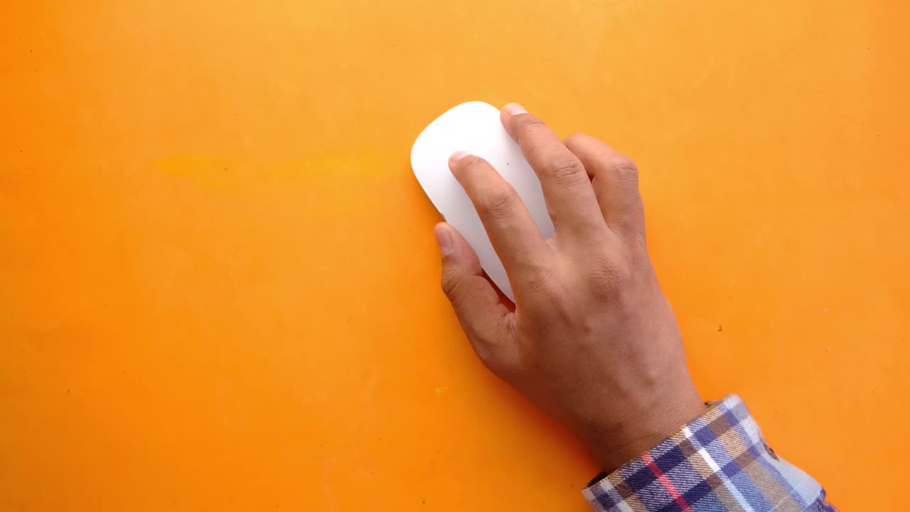 Person using a white computer mouse on an orange surface