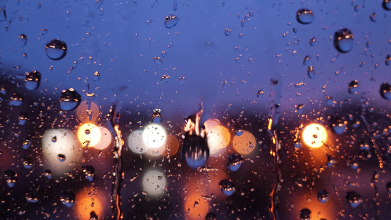 Regndråber på et vindue: En smuk aftenscene fanget gennem et regnvådt glas, der understreger den afslappende stemning af regn og byens bokeh-lys.