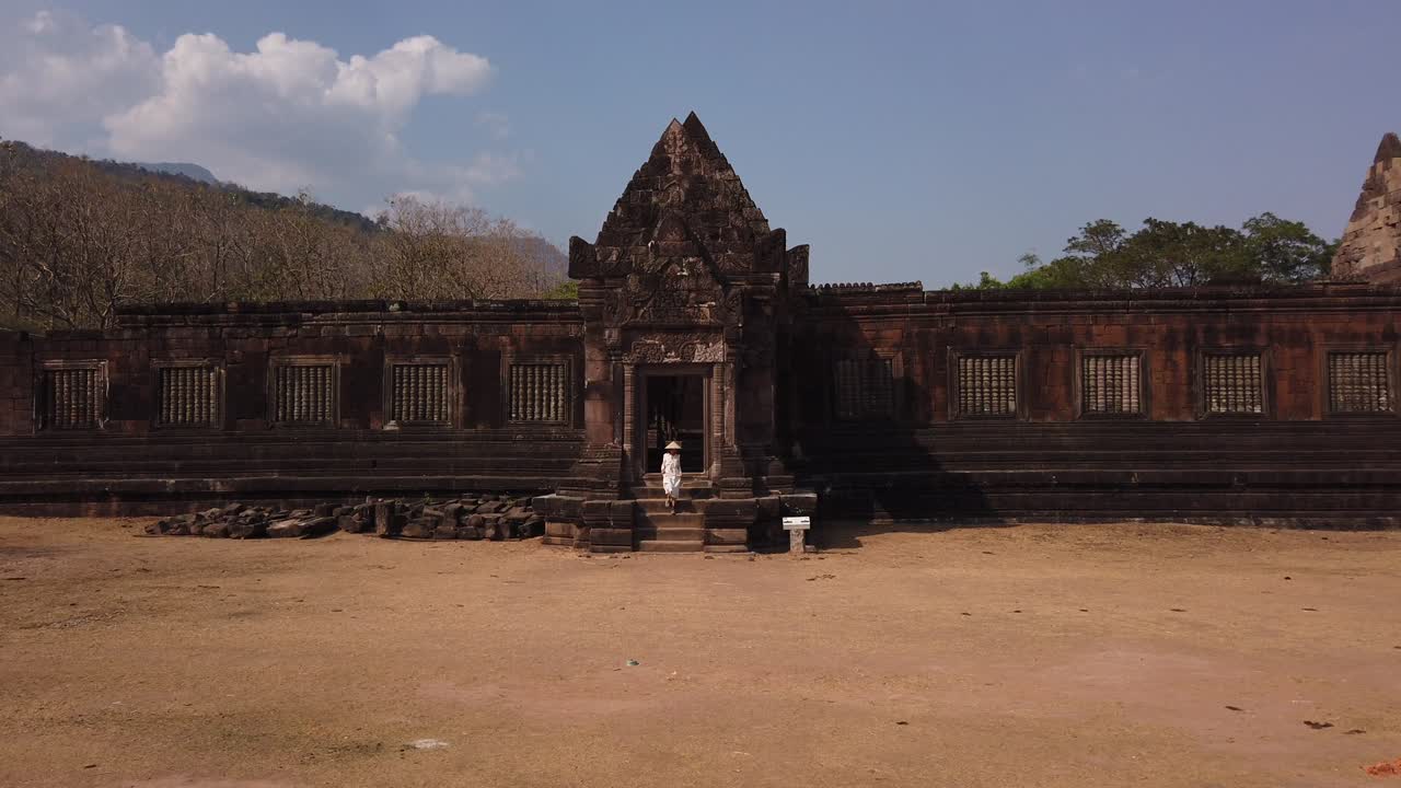 mujer joven hermosa viajera con un largo vestido blanco y sombrero vietnamita sale del palacio khmer en wat phou complejo de templos hindúes en ruinas. champassak, laos, asia. cultura antigua arquitectura religiosa.